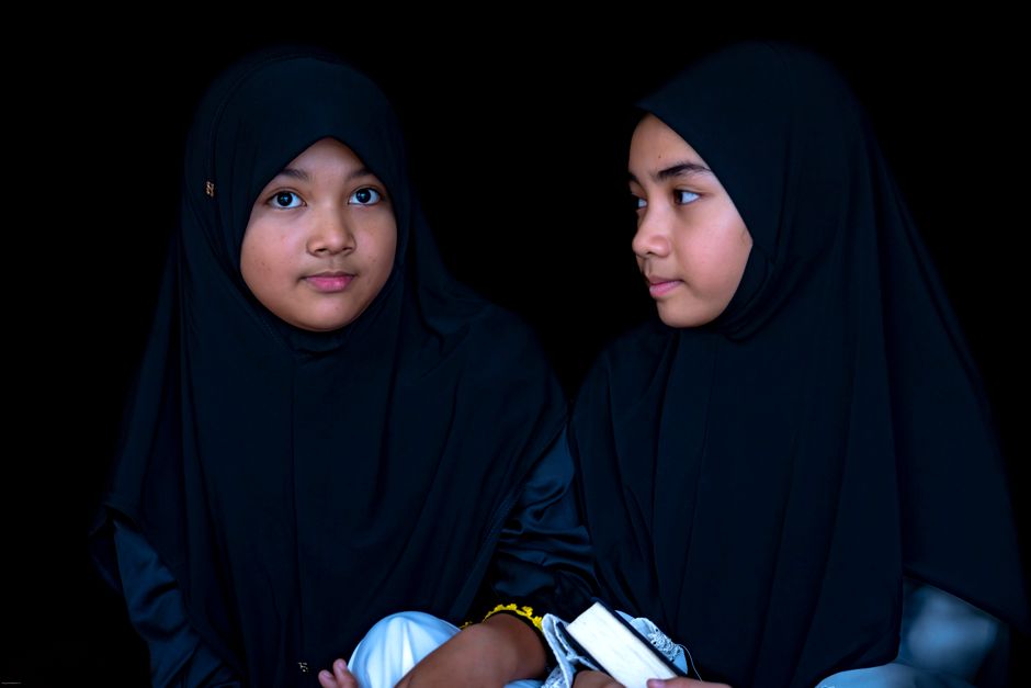 Seorang pemuda Muslim dengan pakaian kasual modern sedang duduk santai di sudut kafe estetik, memegang secangkir kopi hangat sambil tersenyum menatap layar tabletnya yang menampilkan aplikasi Al-Quran digital, menciptakan suasana tenang dan damai.