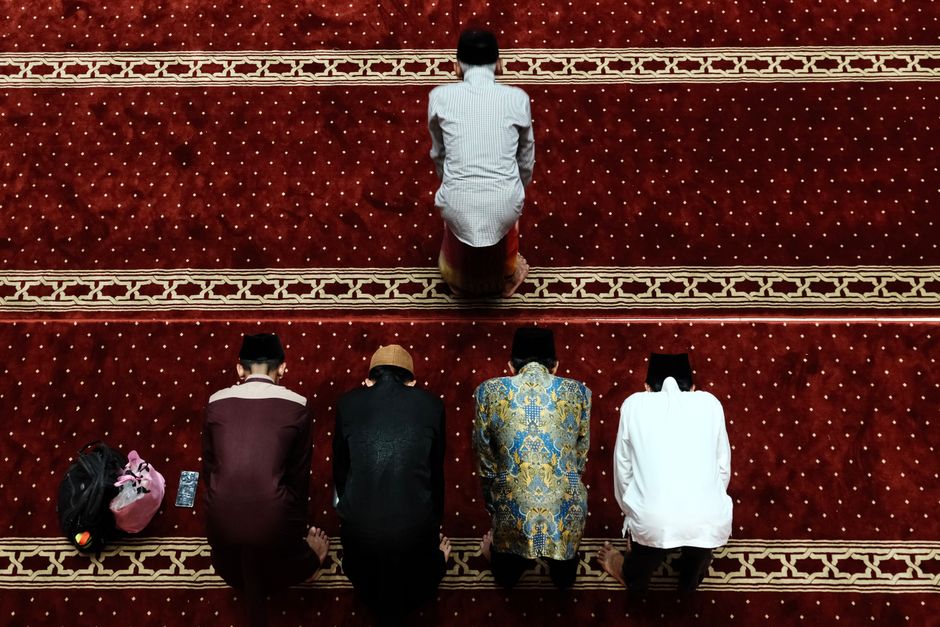 Seorang pemuda Muslim modern sedang duduk santai di sebuah kafe estetik, memegang segelas kopi hangat sambil tersenyum menatap laptopnya yang menampilkan halaman jurnal harian, dengan suasana hangat dan pencahayaan alami yang menenangkan.
