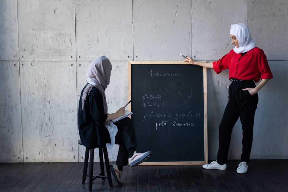 Seorang pemuda Muslim modern mengenakan pakaian kasual rapi sedang duduk santai di sudut kafe yang estetik, memegang cangkir kopi sambil tersenyum tenang menatap laptopnya dengan suasana pencahayaan yang hangat.