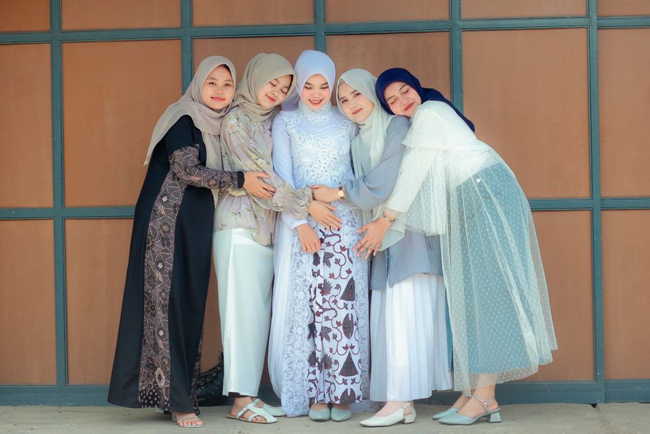 Seorang anak muda Muslim dengan pakaian kasual modern sedang duduk santai di kafe yang estetik, memegang cangkir kopi sambil tersenyum menatap ke luar jendela dengan suasana tenang, hangat, dan estetik.