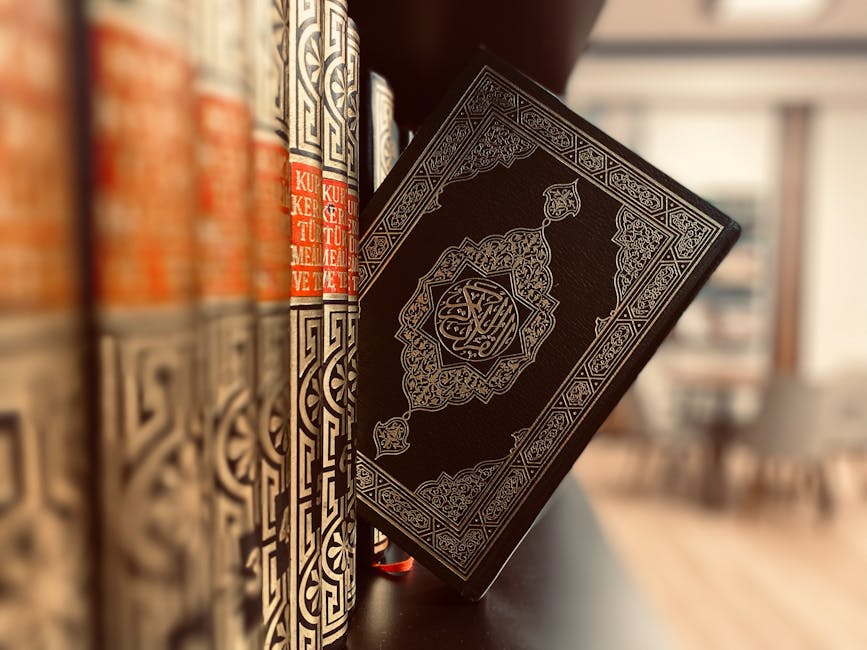 Foto detail kaligrafi ayat Al-Quran pada naskah kuno yang diletakkan di atas meja kayu dengan latar belakang rak buku perpustakaan Islam yang klasik dan tenang.
