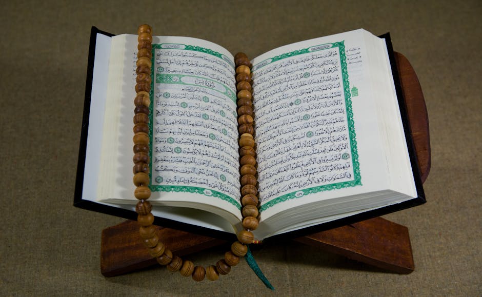 Foto sebuah mushaf Al-Quran terbuka dengan rasm utsmani yang jelas, terletak di atas meja kayu jati tua di dalam perpustakaan klasik yang dipenuhi kitab-kitab kuning, dengan cahaya matahari pagi masuk melalui jendela masjid yang tenang.