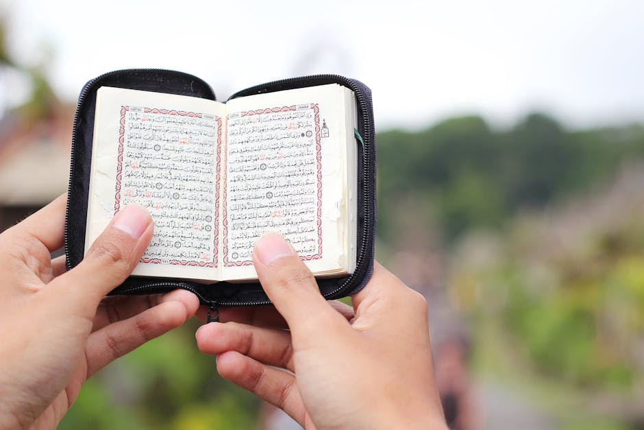 Foto sebuah mushaf Al-Quran kuno yang terbuka di atas meja kayu di dalam perpustakaan klasik dengan cahaya matahari pagi yang masuk melalui celah jendela, memberikan suasana spiritual dan keilmuan yang mendalam.