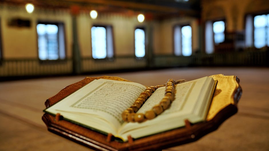 Foto naskah kuno kitab hadis yang terbuka di atas meja kayu dengan pencahayaan hangat, dikelilingi oleh tumpukan kitab klasik di perpustakaan tradisional yang tenang.