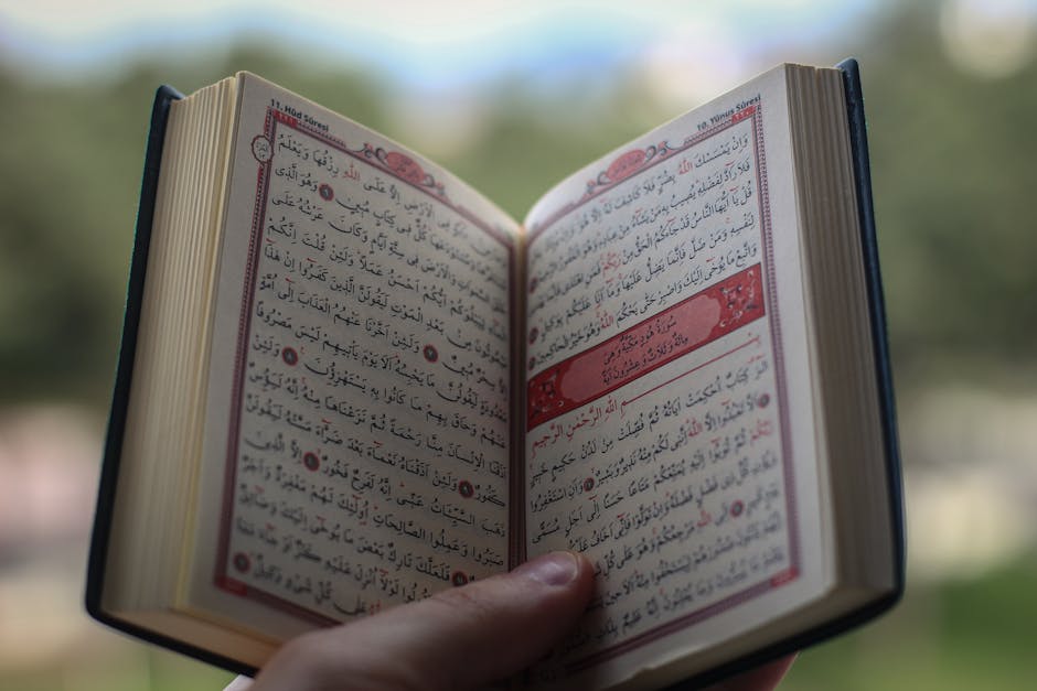 Foto sebuah mushaf Al-Quran terbuka di atas meja kayu di dalam perpustakaan klasik dengan cahaya hangat yang masuk dari jendela, dikelilingi oleh kitab-kitab turats tebal yang melambangkan kedalaman ilmu pengetahuan Islam.