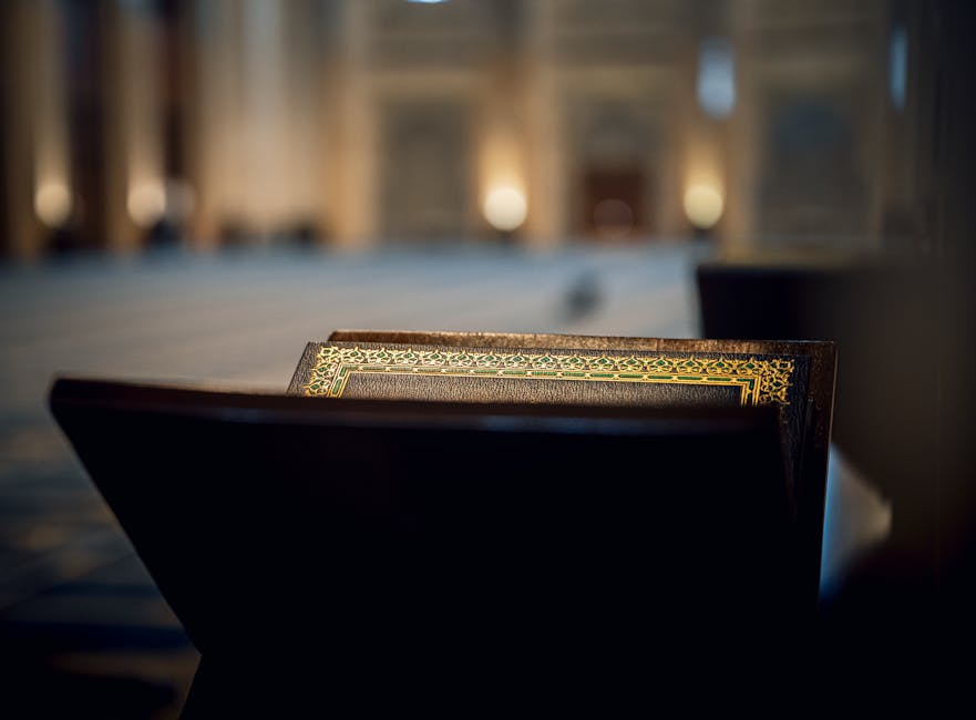 Foto sebuah mushaf Al-Quran klasik yang terbuka pada halaman Surah Al-Ikhlas dengan latar belakang rak buku perpustakaan Islam yang penuh dengan kitab-kitab turats tebal, menciptakan suasana keilmuan yang mendalam dan tenang.