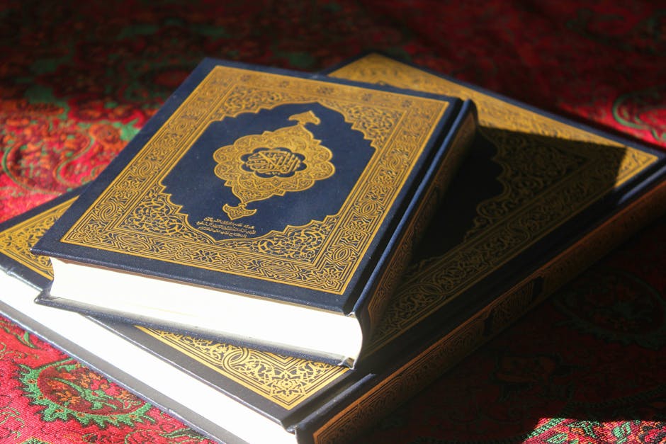 Foto sebuah naskah kuno kitab hadits dengan tulisan kaligrafi Arab yang indah di atas meja kayu tua, dikelilingi oleh tumpukan kitab-kitab klasik di sebuah perpustakaan Islam yang tenang dengan pencahayaan hangat.