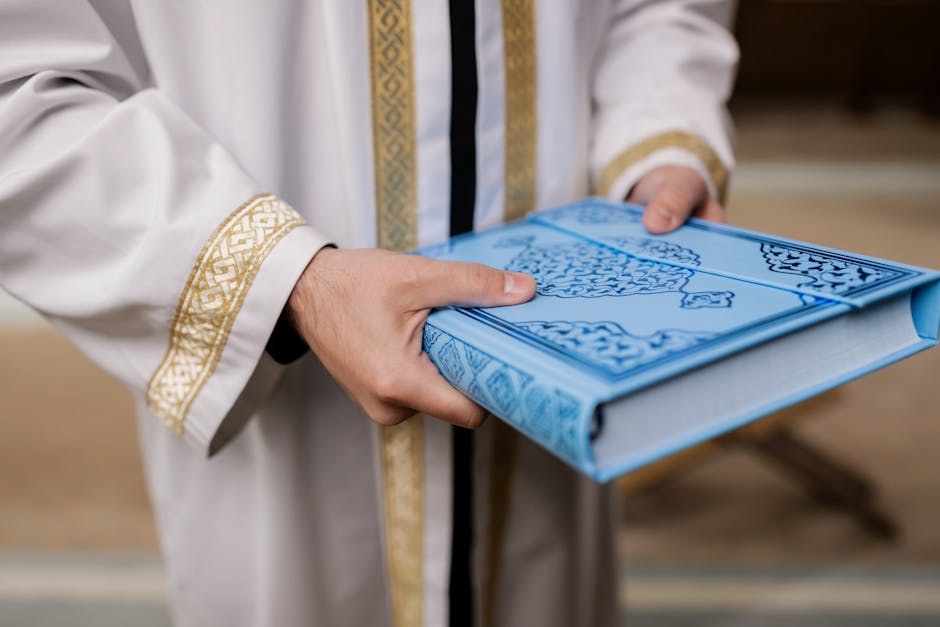 Foto sebuah naskah hadis kuno dengan tulisan kaligrafi Arab yang indah di atas meja kayu tua, dikelilingi oleh tumpukan kitab-kitab klasik di dalam perpustakaan Islam yang memiliki pencahayaan hangat.