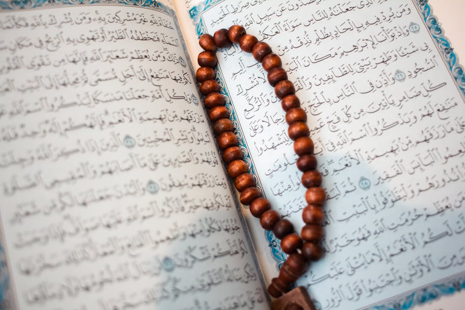 Foto mushaf Al-Quran terbuka dengan pencahayaan lembut di atas meja kayu di dalam perpustakaan klasik Islam, dikelilingi oleh kitab-kitab turats yang tebal, menciptakan suasana ilmiah dan spiritual yang mendalam.