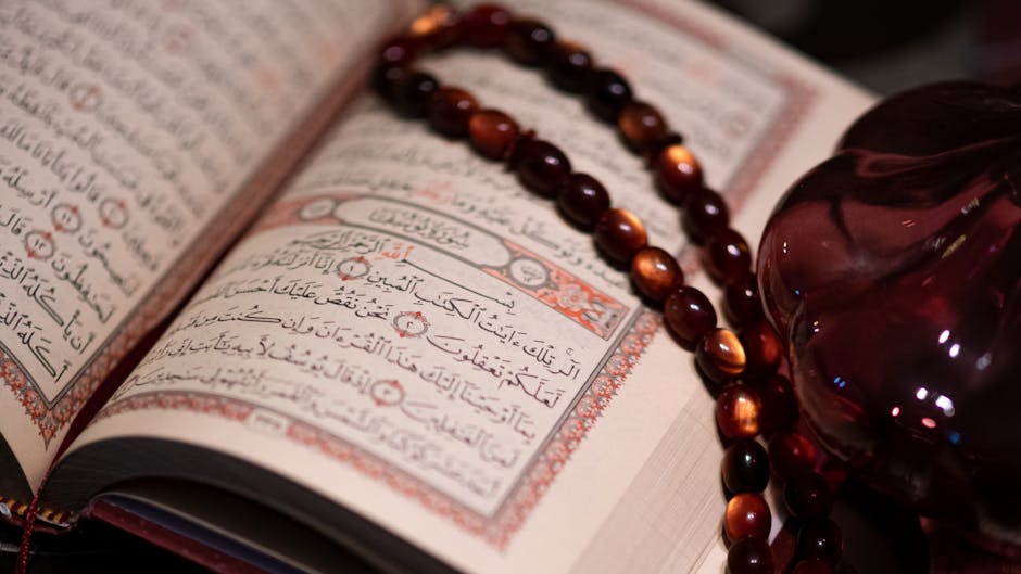 Foto sebuah naskah kuno kitab hadis yang terbuka di atas meja kayu di dalam perpustakaan klasik dengan pencahayaan hangat, dikelilingi oleh tumpukan kitab-kitab turats yang berwibawa.
